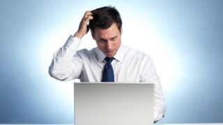A businessman looking at a laptop and scratching his head